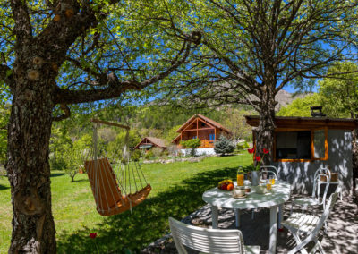Le Chalet Carpe Diem le jardin en été avec sa terrasse ombragée et cuisine d'été